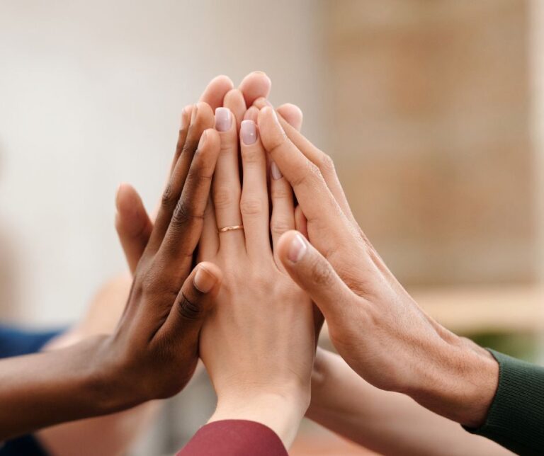Mehrere Hände berühren sich in einer warmen Geste – Symbol für Nähe, Mitgefühl und Unterstützung bei ungewollter Kinderlosigkeit.