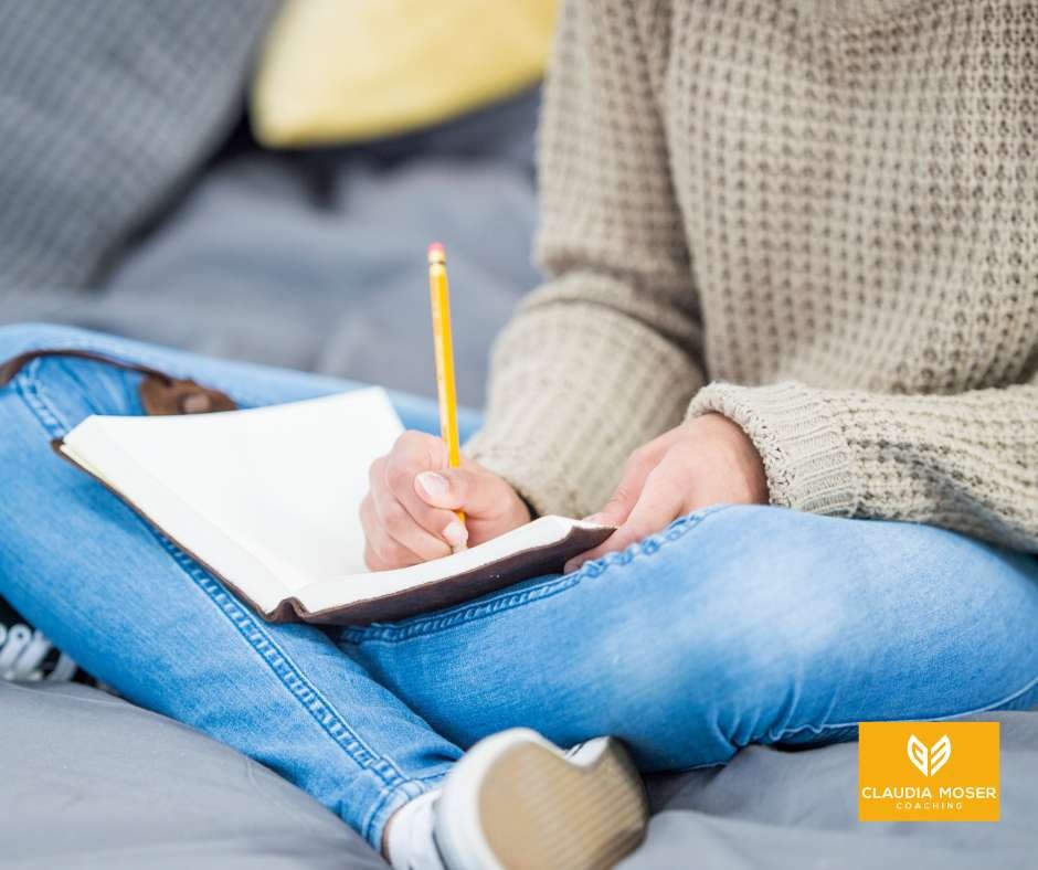 Frau sitzt auf dem Bett und schreibt mit Stift in ein Journal